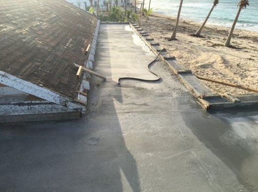 The roof from above, the fresh slab, and the palms stripped bare by the storm.